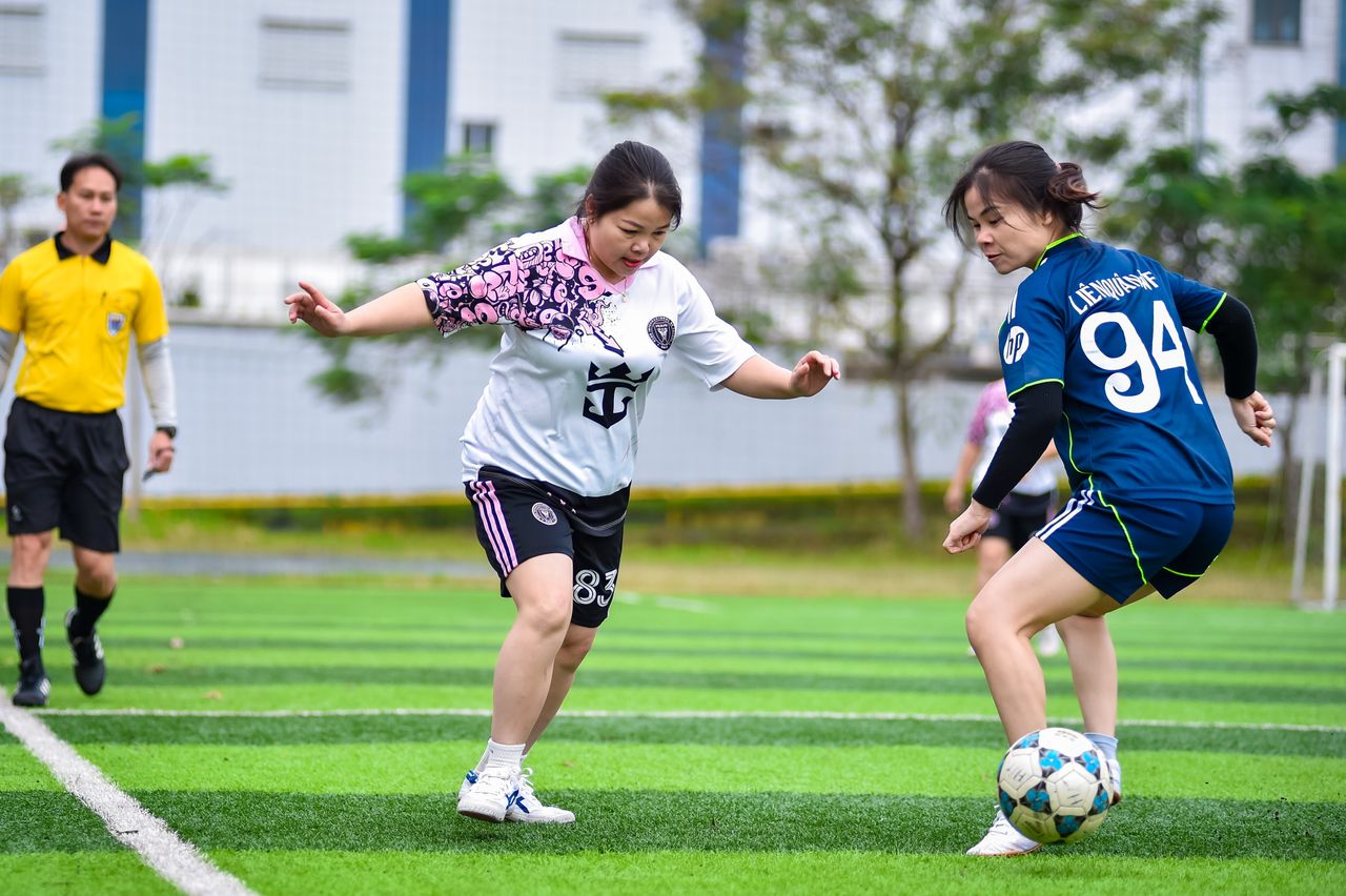 Women playing a competitive football match outdoors in Hanoi.